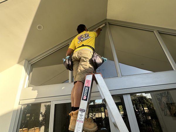Cleaner on a ladder detailing high entryway windows