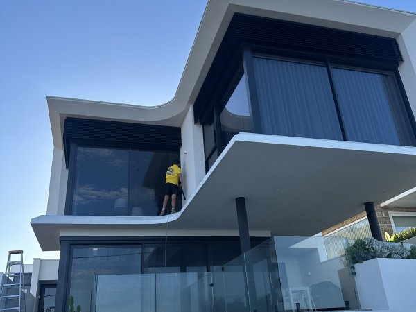 Cleaner working on the balcony windows of a modern two-storey home