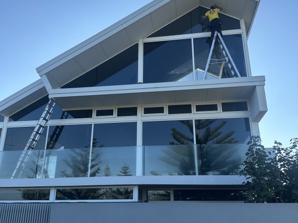 Cleaner on a ladder reaching apex windows on a coastal home