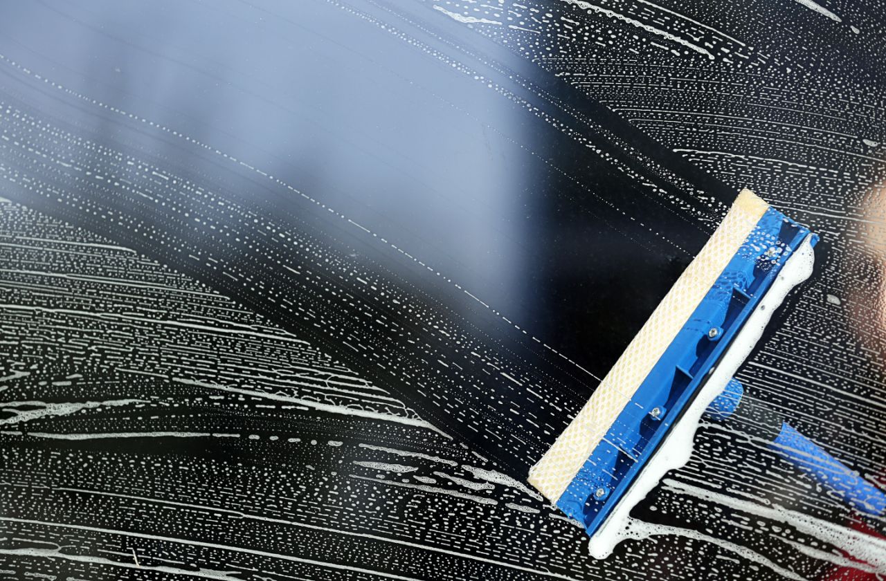 Squeegee pulling foam across dark glass